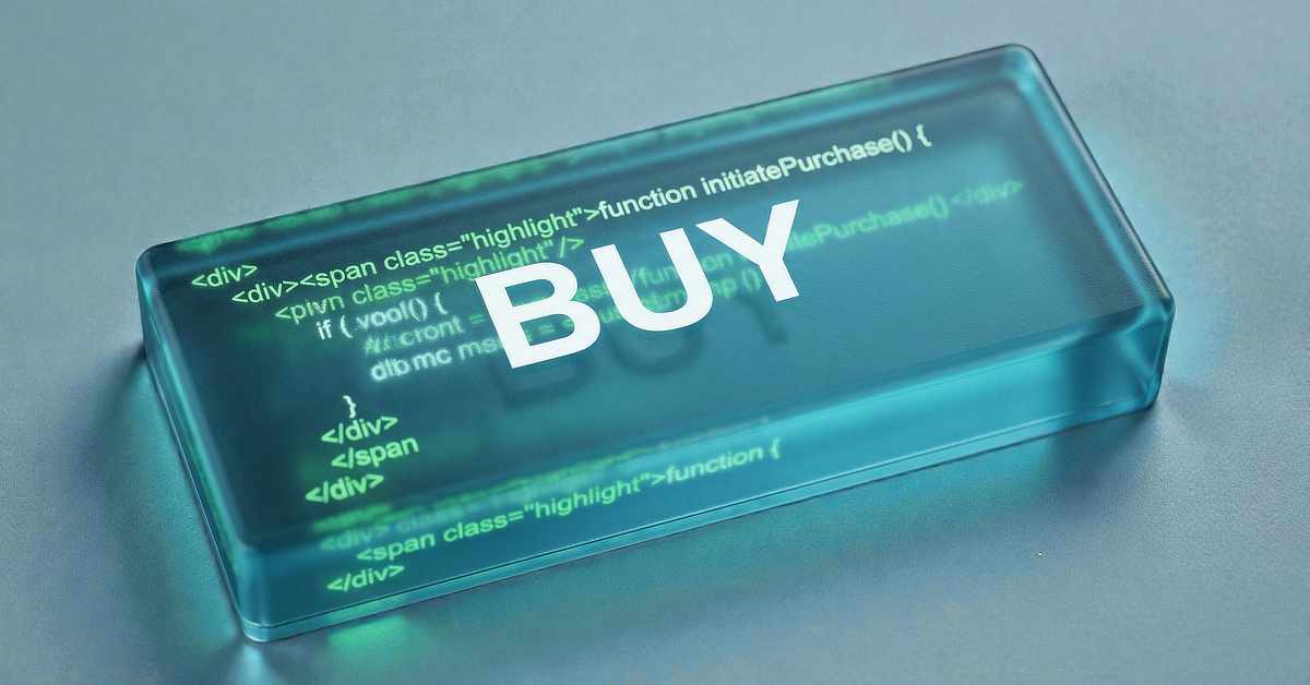 A close-up of a translucent, glass-like rectangular button labeled “BUY” in large white letters. Beneath the surface, faint green programming code is visible, suggesting a digital or e-commerce interface. The button rests on a neutral surface with soft lighting and a shallow depth of field.